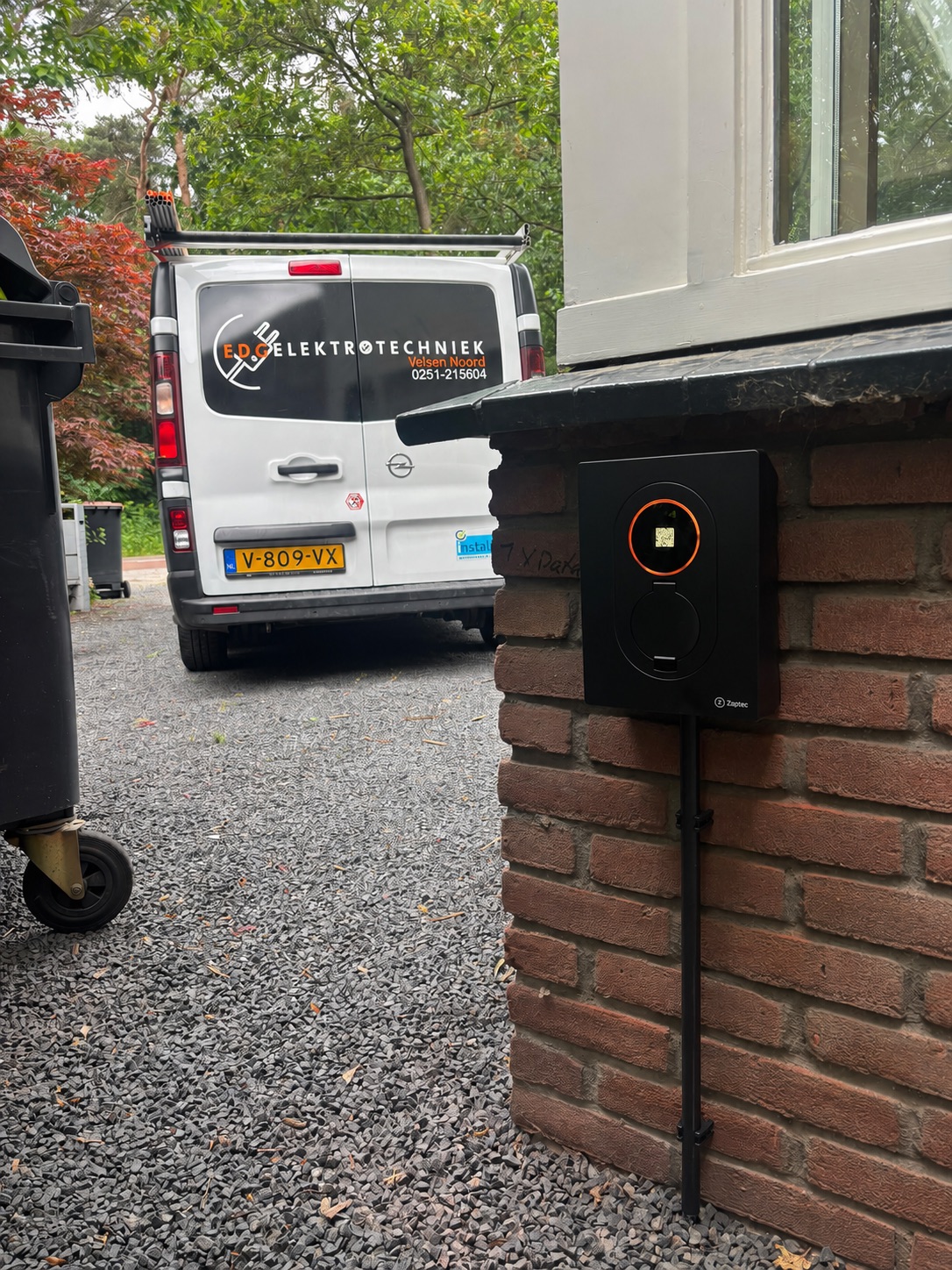 Zaptec laadpaal gemonteerd op een bakstenen muur, met op de achtergrond een bestelbus van EDC Elektrotechniek uit Velsen Noord