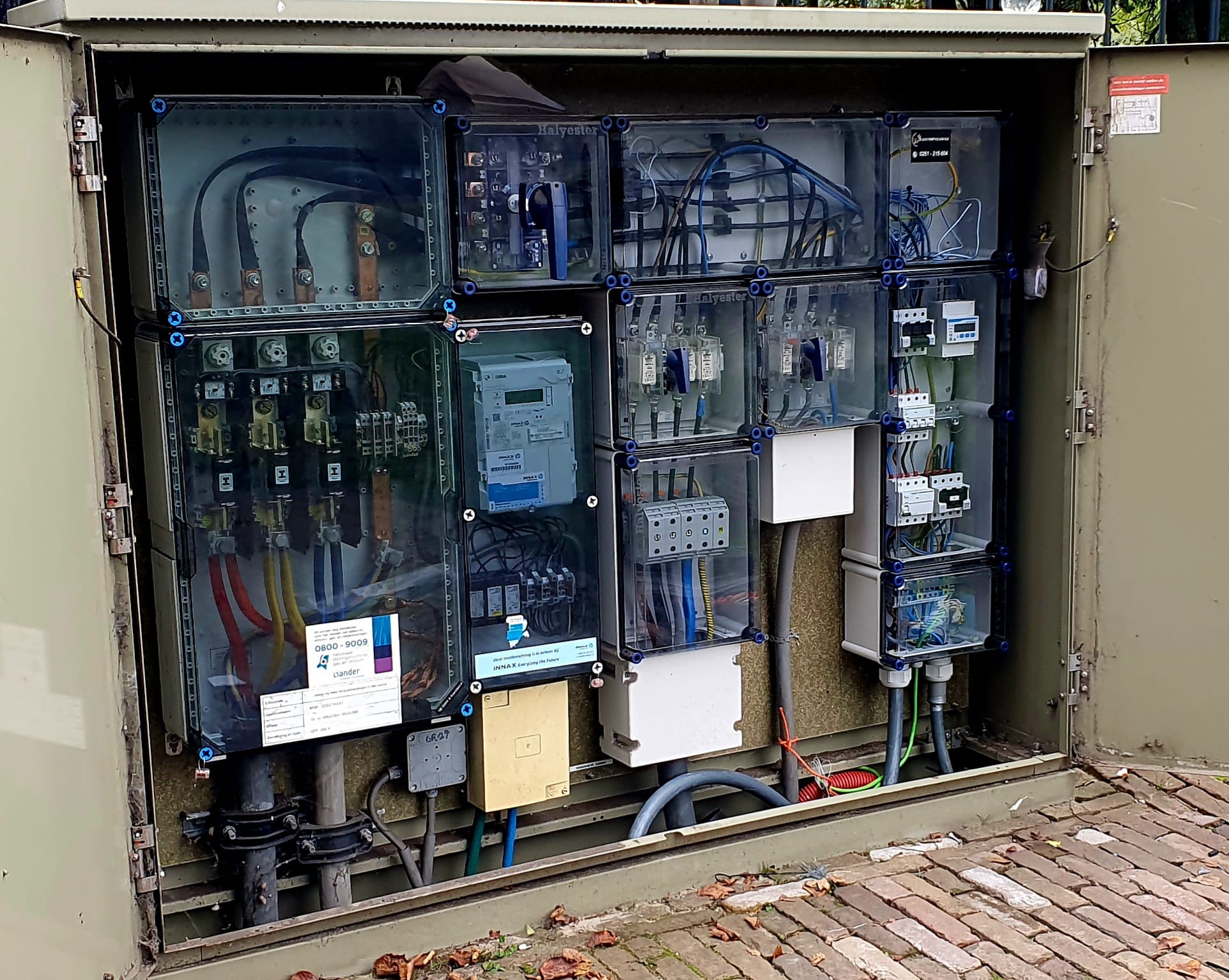 Openstaande elektriciteitskast met zekeringen, meters en bekabeling van Innax en Liander op straat