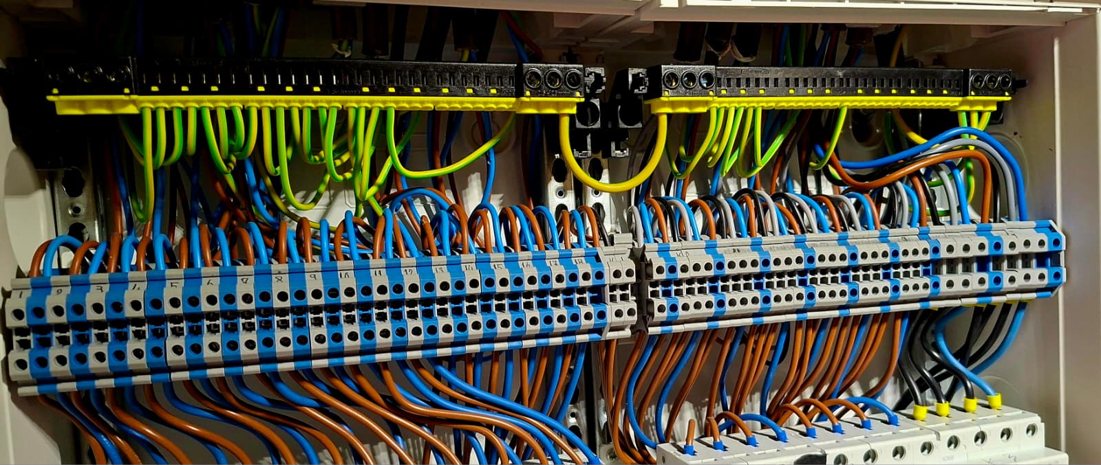 Elektrische schakelkast met genummerde klemmenstroken en gekleurde bedrading in blauw, bruin en groen-geel