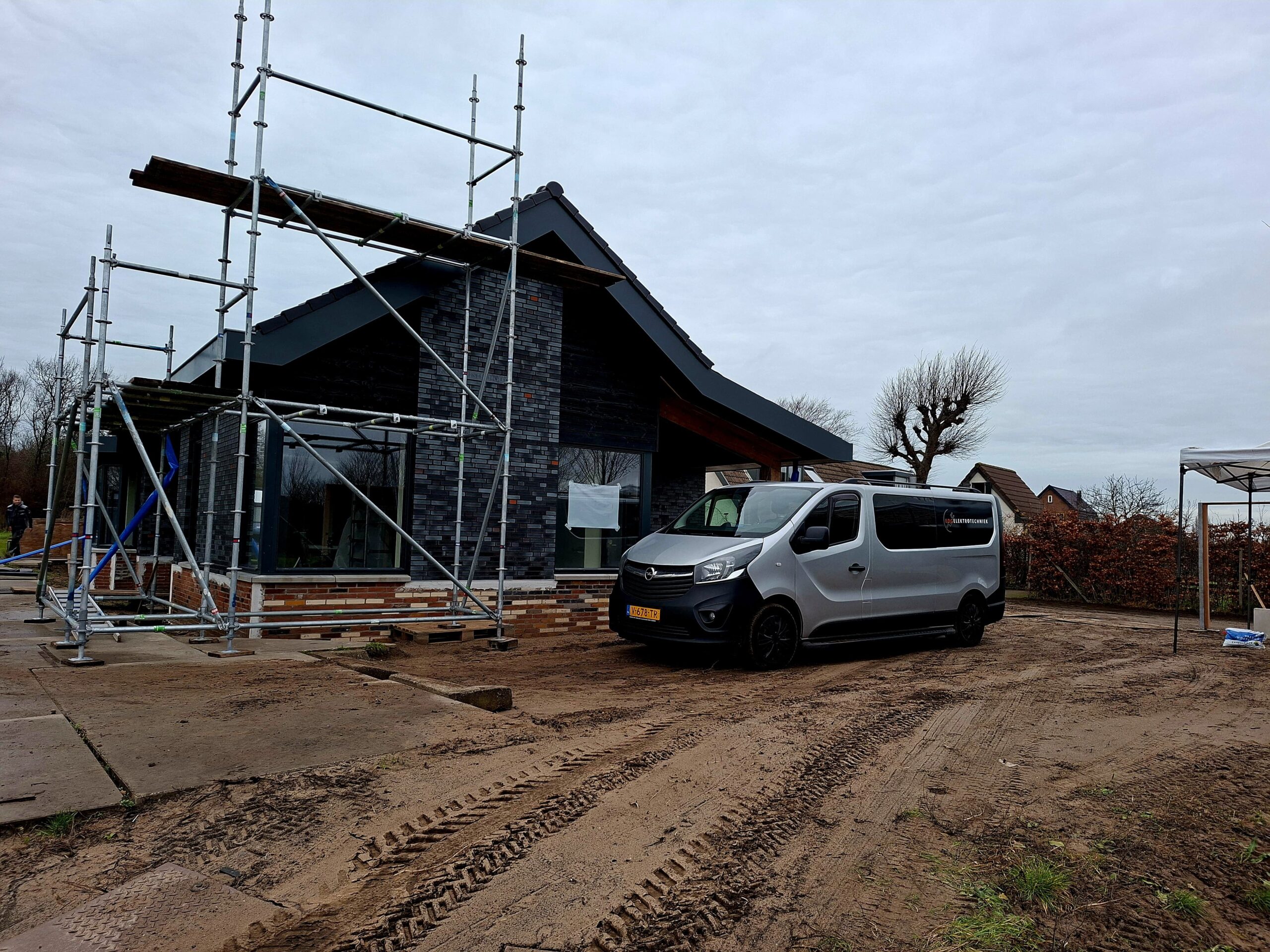 Nieuwbouwwoning in aanbouw met steiger en een zilveren bedrijfsbus van een elektrotechnisch bedrijf op de bouwplaats