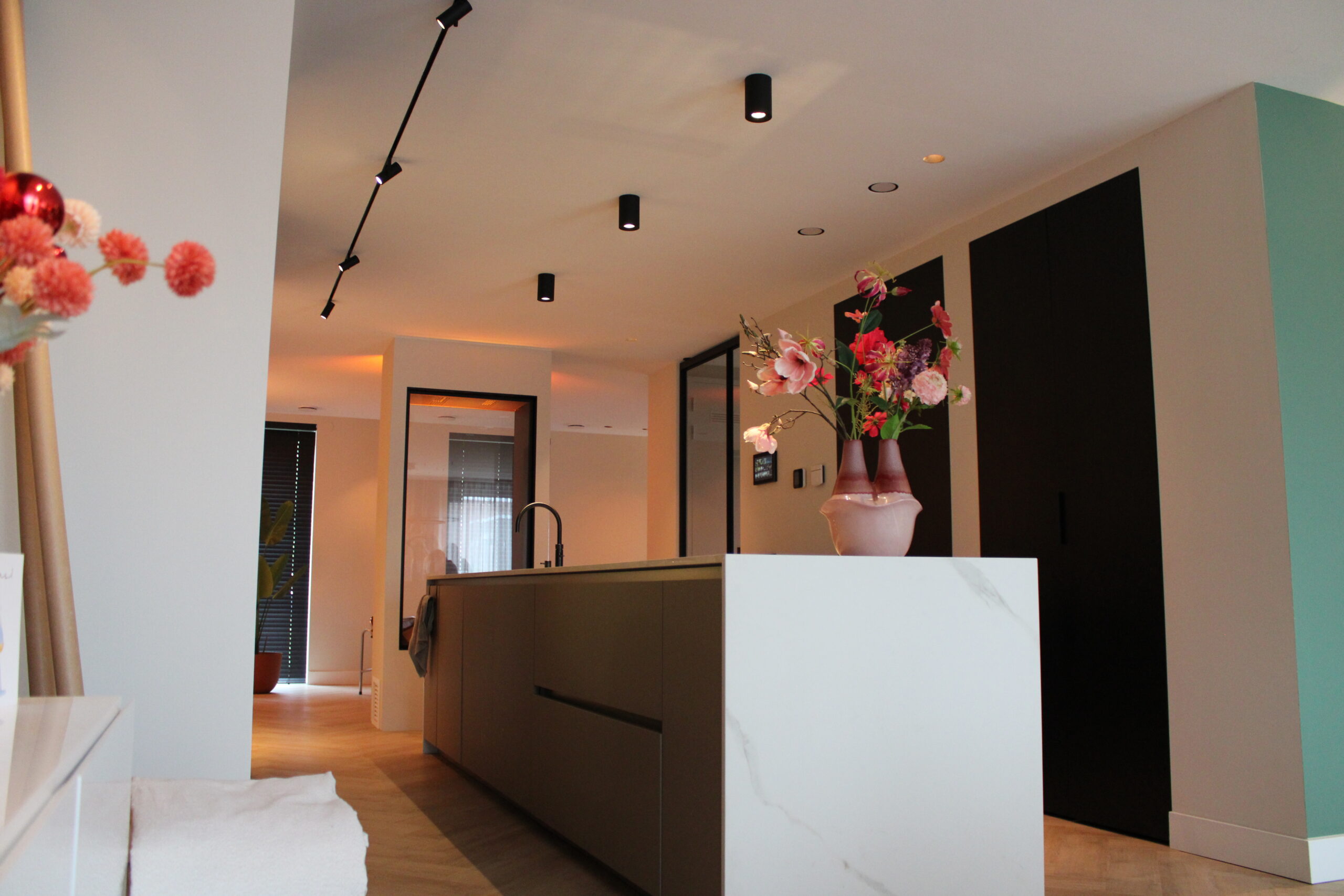 Modern open keuken met donker keukeneiland, marmeren werkblad, roze bloemen in vaas en zwarte plafondspots
